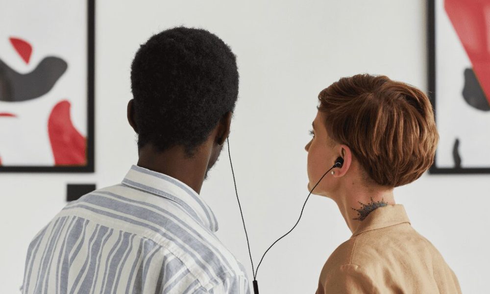 Two people looking at art and listening to shared earbuds.