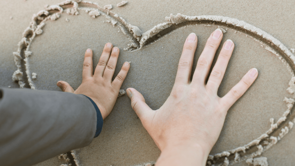 two hands in a heart drawn in the sand