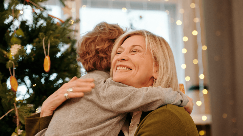 Woman hugging child in front of Christmas tree.