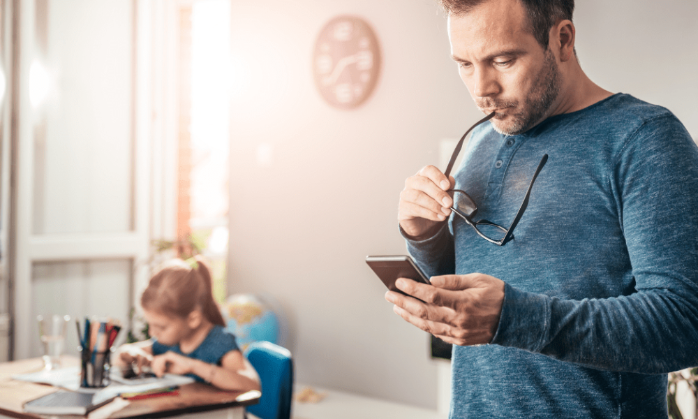 man on smart phone while daughter studies nearby